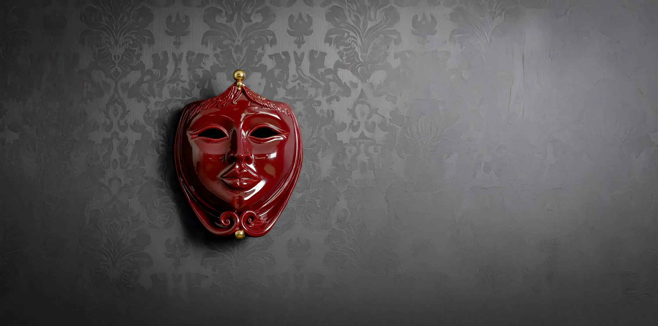 Maschera in ceramica di Caltagirone rossa lucida con dettagli dorati su parete grigia decorata, fatta a mano