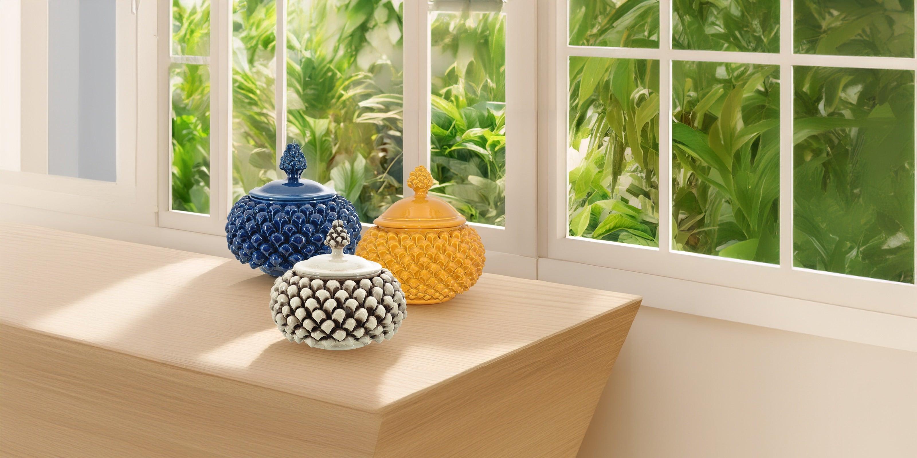 Biscottiere a pigna ceramiche di Caltagirone fatti a mano, colorate, su tavolo davanti a finestra.