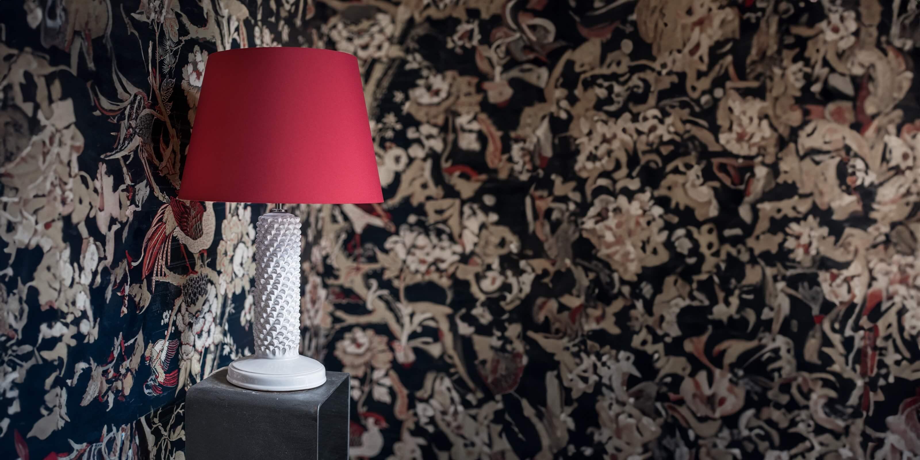 Lampada con base in ceramica di Caltagirone fatta a mano e paralume rosso su mobiletto davanti a parete decorata