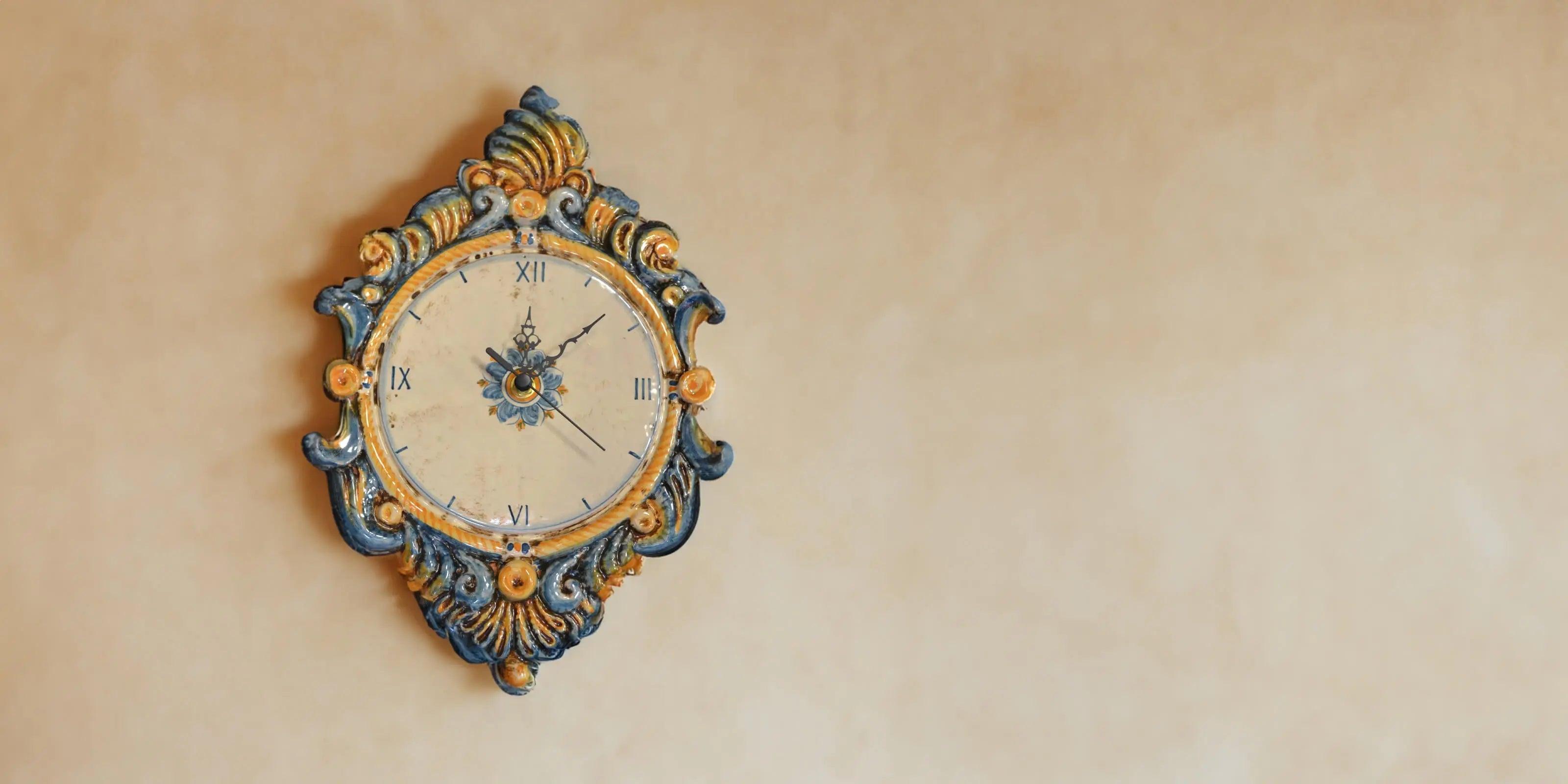 Orologio in ceramica di Caltagirone fatto a mano con decorazioni blu e gialle su muro beige