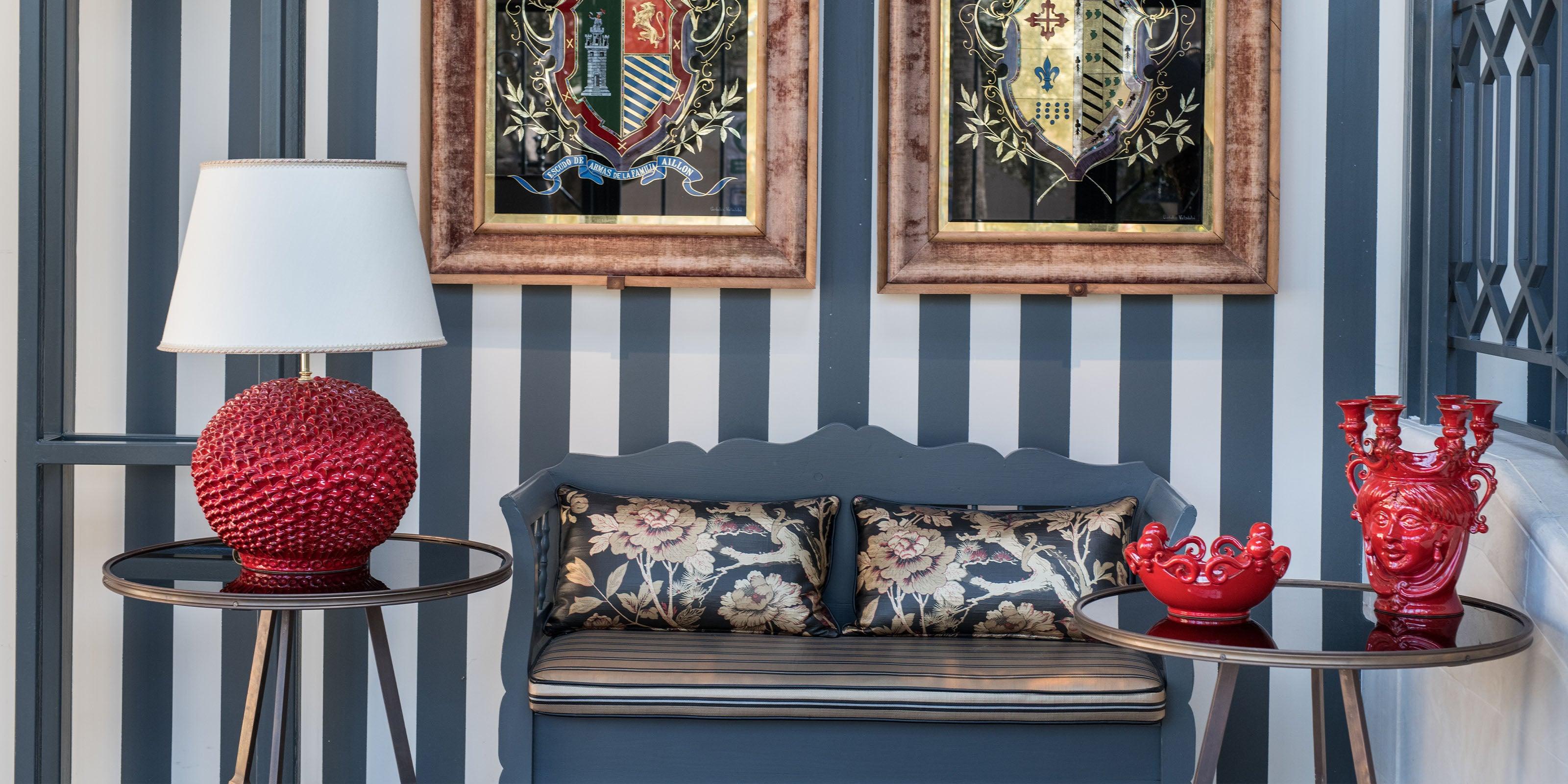 Ceramiche di Caltagirone fatti a mano rosso fuoco su tavoli con lampada e divanetto elegante con cuscini floreali