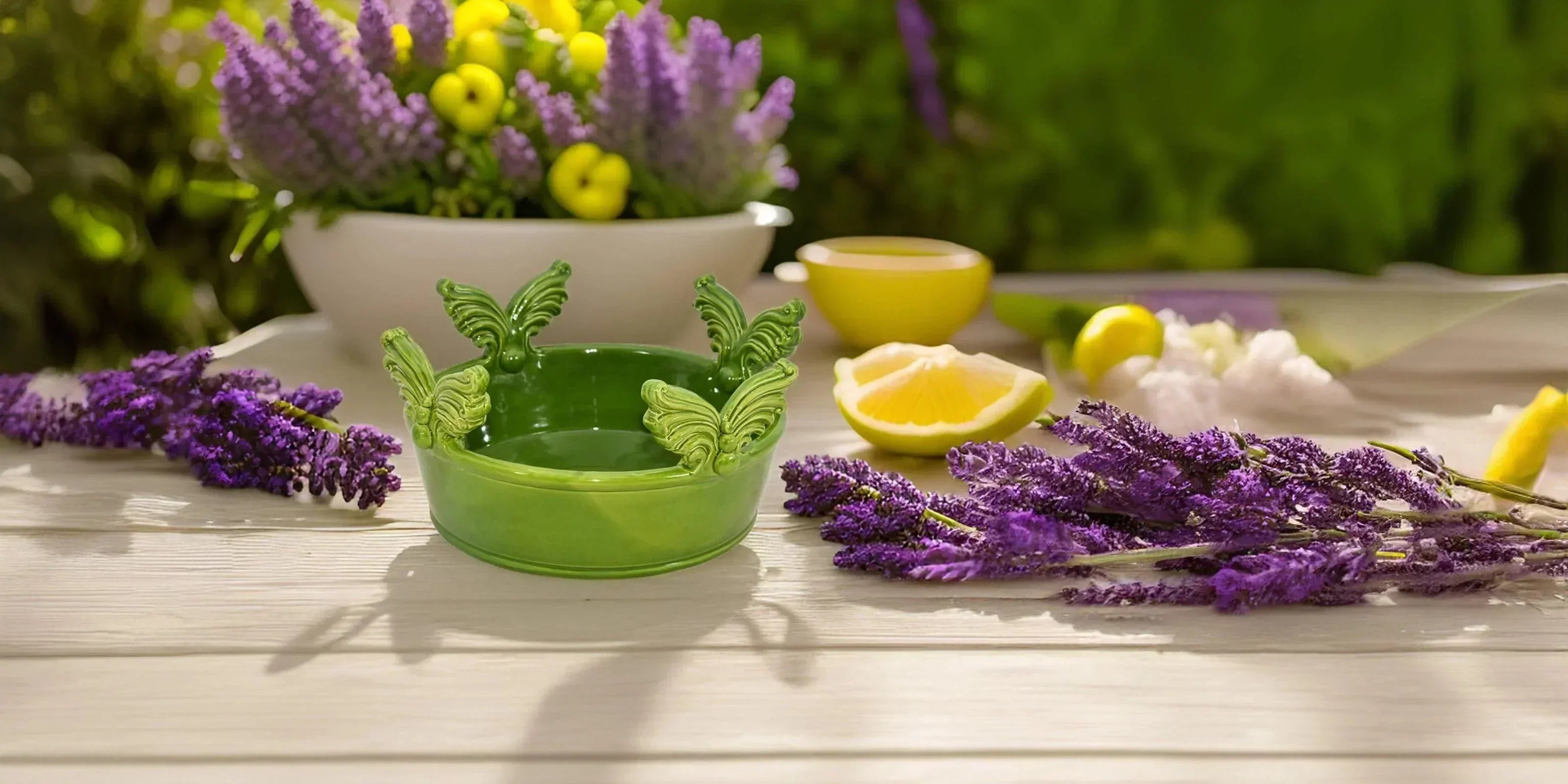 Ceramiche Caltagirone fatti a mano, ciotola verde con farfalle accanto a fiori viola e limoni su tavolo chiaro