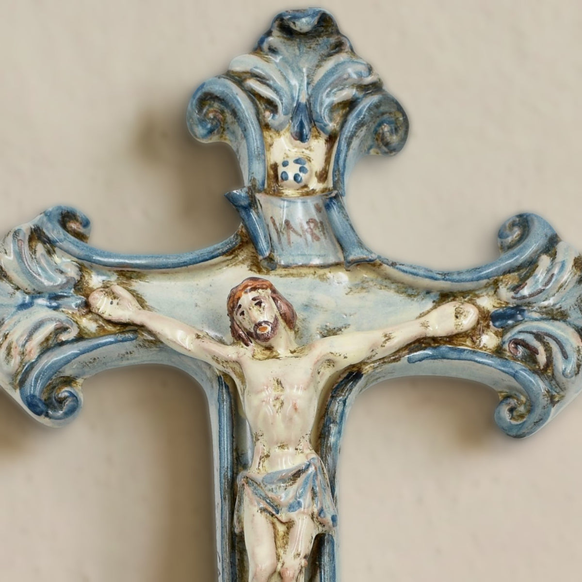 Dettaglio del crocifisso in ceramica di Caltagirone Mono Blu appeso alla parete: Cristo in rilievo, cartiglio INRI e cimasa a volute blu