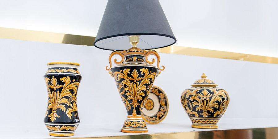 Ceramiche Caltagirone fatti a mano: vaso, lampada e barattolo decorati a mano con motivi tradizionali su sfondo nero e oro.