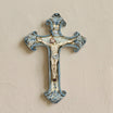 Crocifisso in ceramica di Caltagirone Mono Blu appeso a una parete chiara, fatto a mano con Cristo in rilievo e volute dipinte in blu